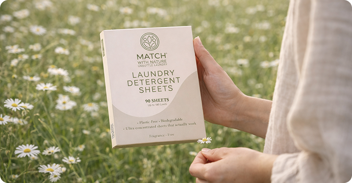 Hand holding a package of Match laundry detergent sheets against a natural background