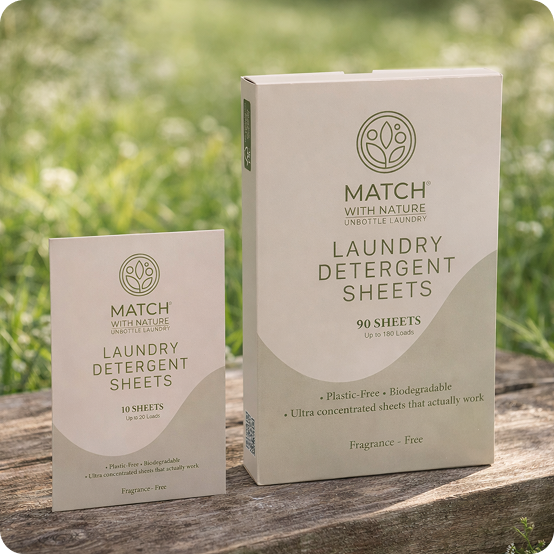Two boxes of Match with Nature laundry detergent sheets on a wooden surface with a grassy background.